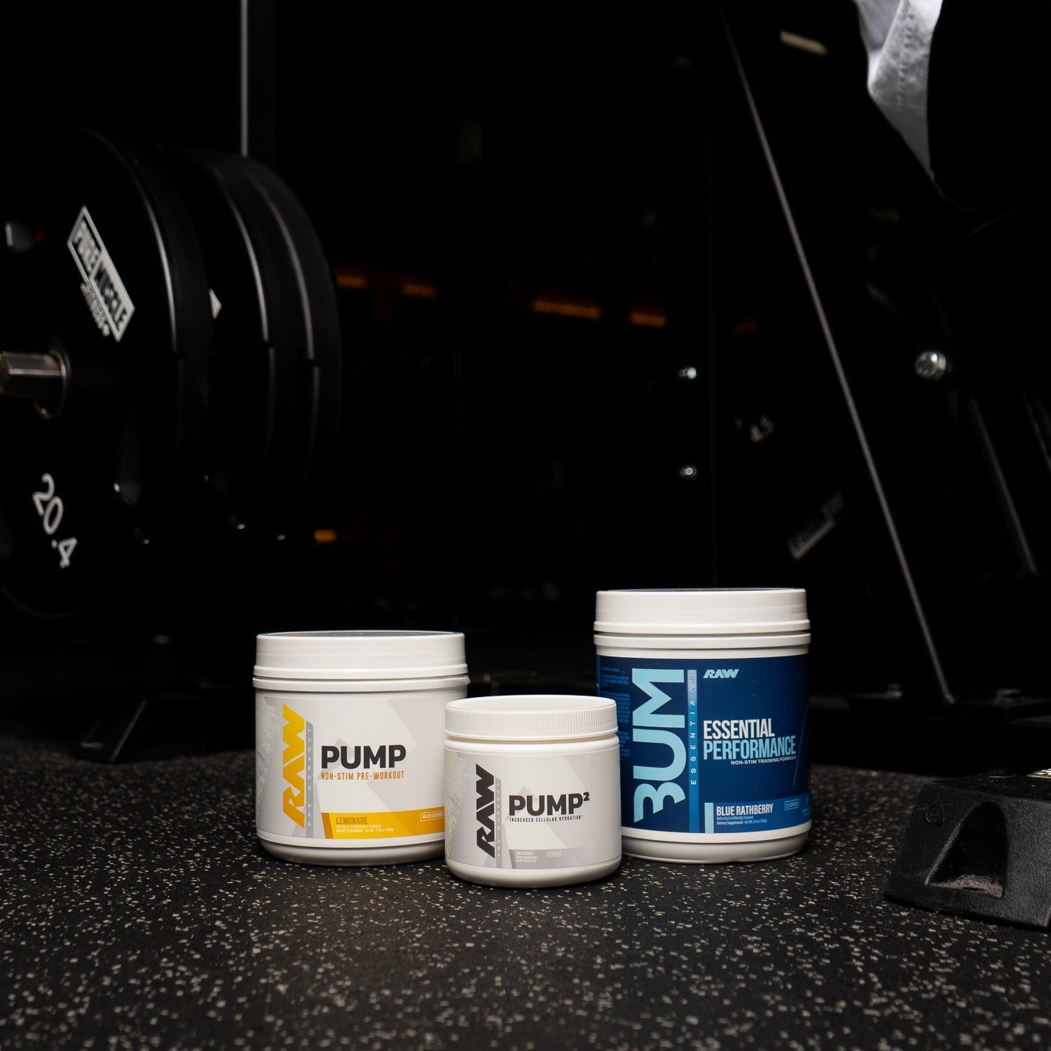 RAW Pump, Pump², and Essential Performance supplements are displayed on a gym floor, with weight plates and equipment in the background.